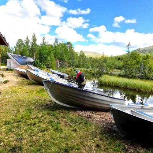 Rad av aluminiumbåtar vid strand, man förbereder utrustning