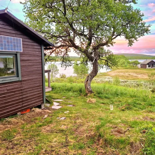 Stuga med solpanel och björk vid sjön i skymning
