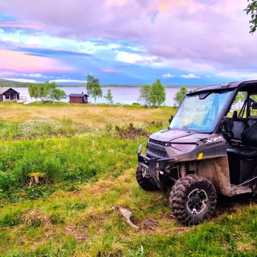 Fyrhjuling parkerad vid sjön med stugor i bakgrunden