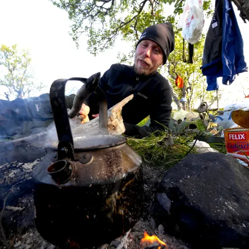 Man kokar kaffe över lägereld i skogen