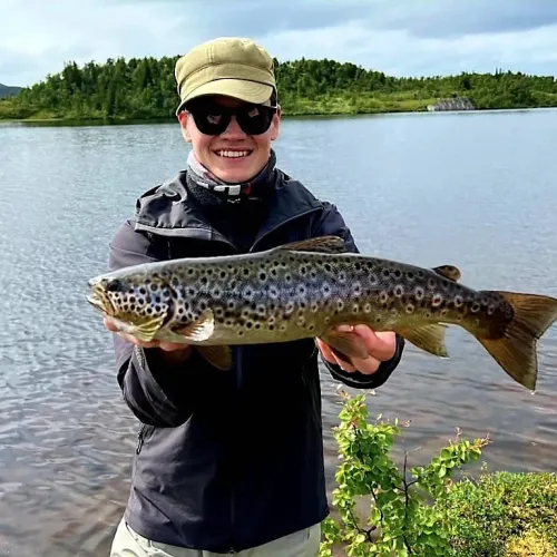 Leende man med keps håller upp stor öring