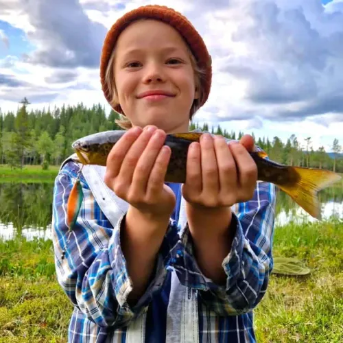 Pojke i mössa håller upp fångad fisk