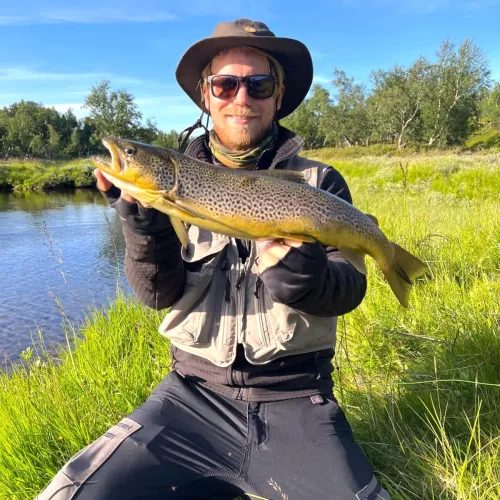 Man i hatt håller stor öring vid ån
