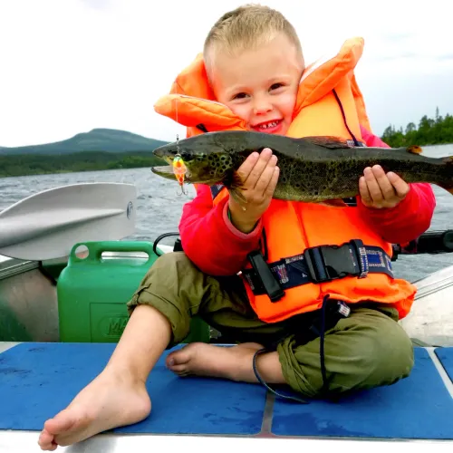 Barfota pojke i flytväst visar fångad fisk