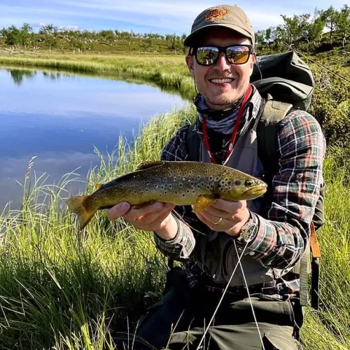 Man med ryggsäck håller öring vid fjällsjö