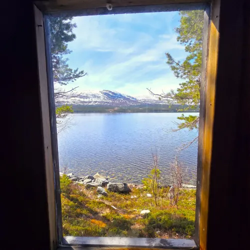 Utsikt genom fönster mot sjö och fjäll