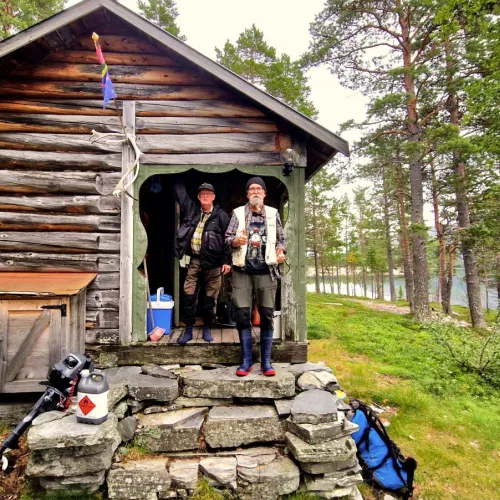 Två män i fiskeutrustning på stugans trapp