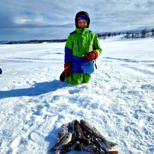Pojke sitter vid sin fångst av fjällfisk på isen