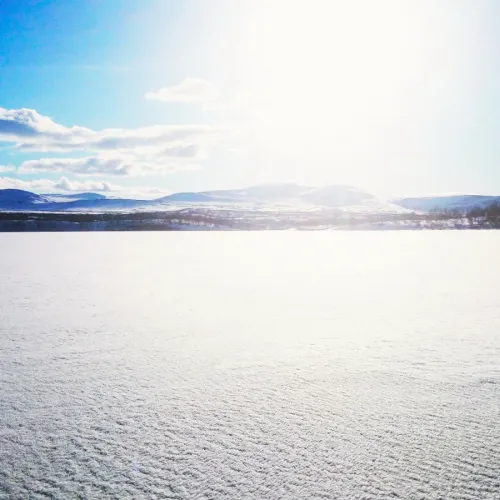 Solblänk över isbelagd fjällsjö med berg i fjärran